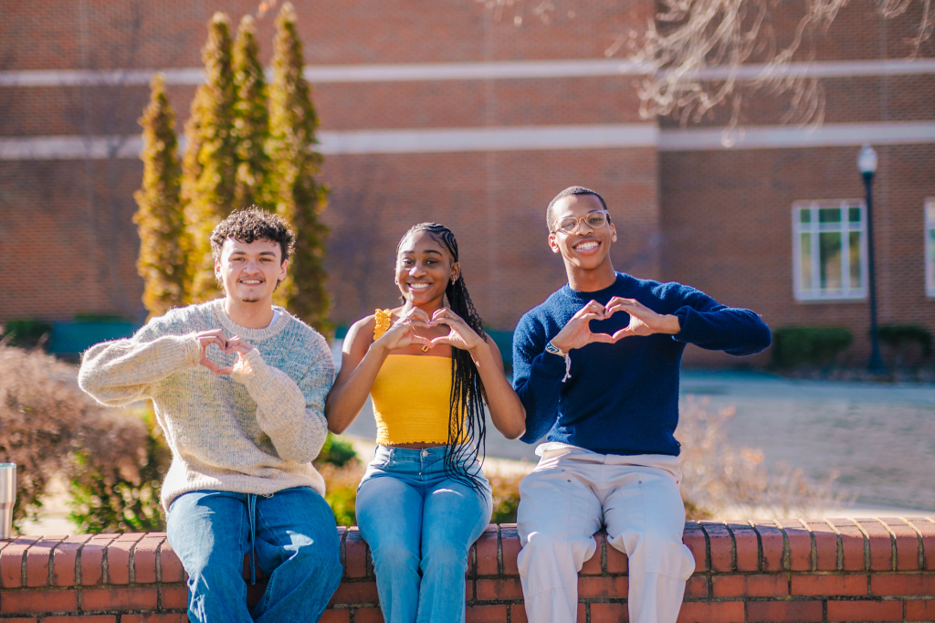 three students smiling and making a heart shape with their hands