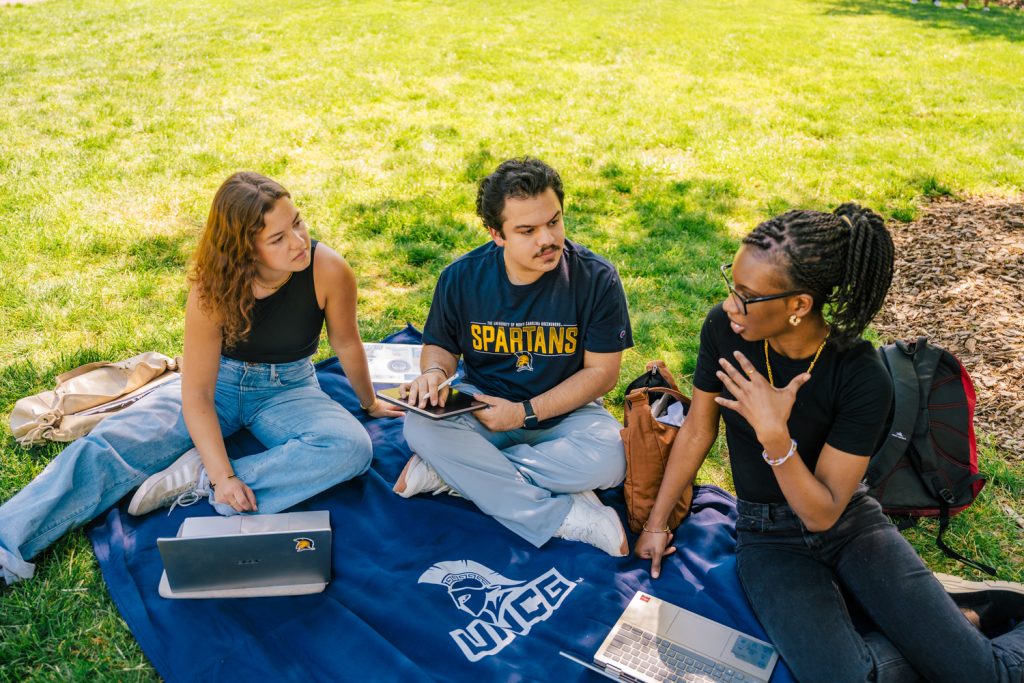 students socializing and relaxing outside of a UNCG campus building on a beautiful spring day.